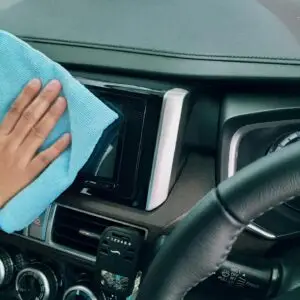 Close-up of a hand cleaning a car dashboard with a blue microfiber cloth.