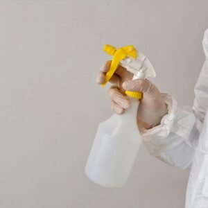 Person in protective gear holding a spray bottle inside a laboratory setting.