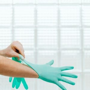 Close-up of a healthcare professional wearing teal gloves against a bright background.